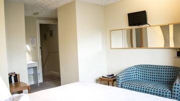 Ein Hotelzimmer mit einem Bett, einem Schreibtisch mit Lampe, einem Sessel und einem an der Wand befestigten Fernseher sowie einem Spiegel über dem Sessel.