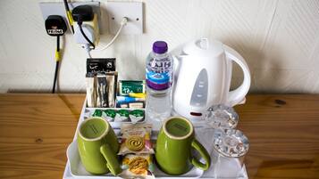 Una bandeja con dos tazas verdes, una botella de agua, una caja de té, un frasco de mermelada y una tetera eléctrica blanca sobre una mesa de madera.