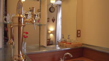 A bathroom with a sink, a mirror, and a glass shelf with bottles.