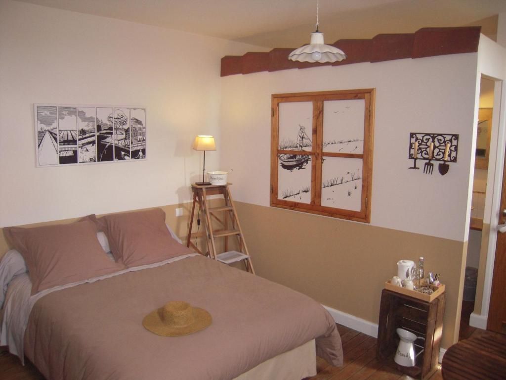 Une chambre avec un lit, une échelle, une fenêtre et des œuvres d’art mural.