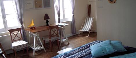 Una habitación con cama, escritorio, dos sillas, lámpara y ventana con cortinas.