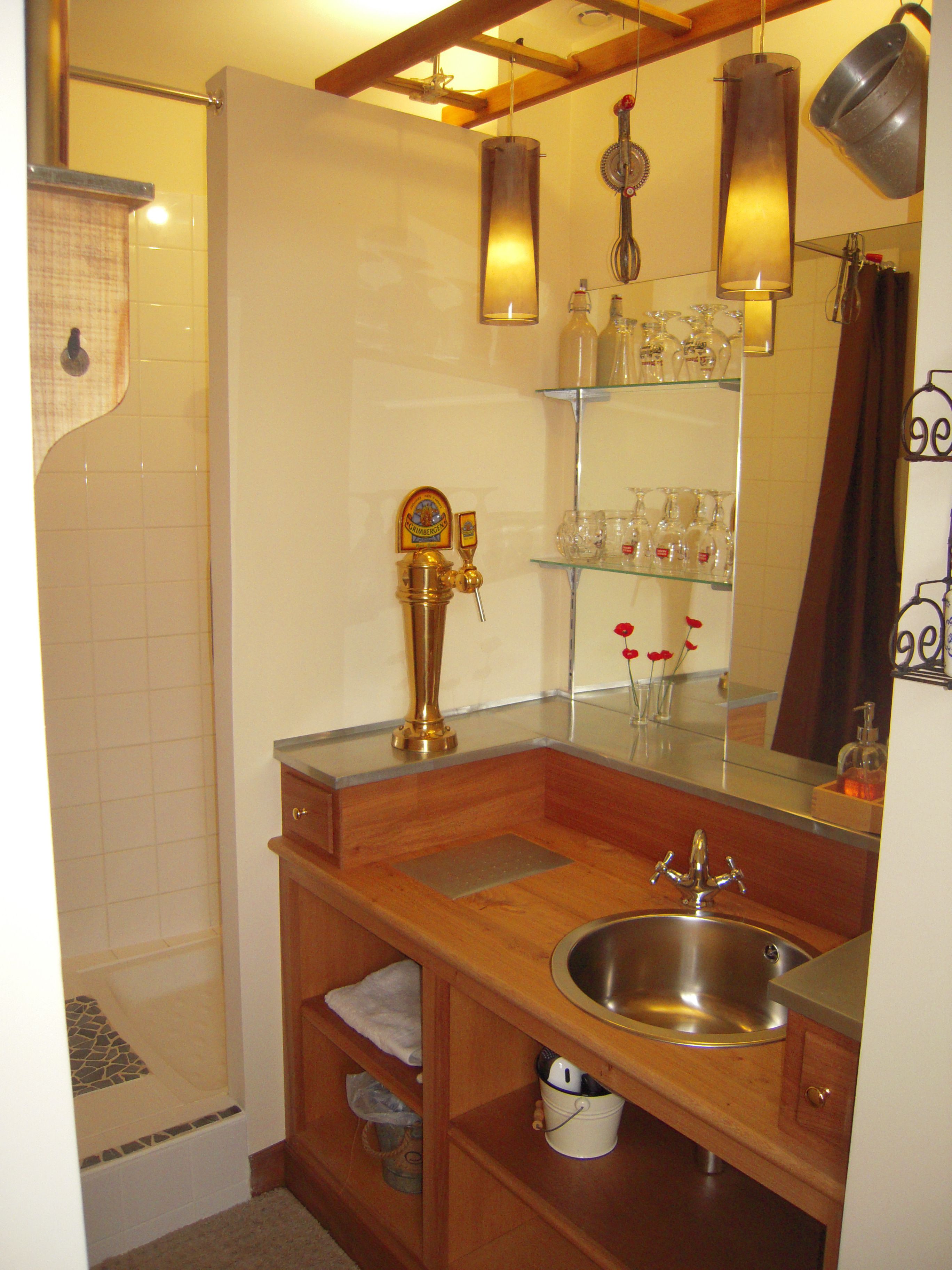 A bathroom with a wooden vanity, a stainless steel sink, a shower with a glass door, and a mirror with shelves above.