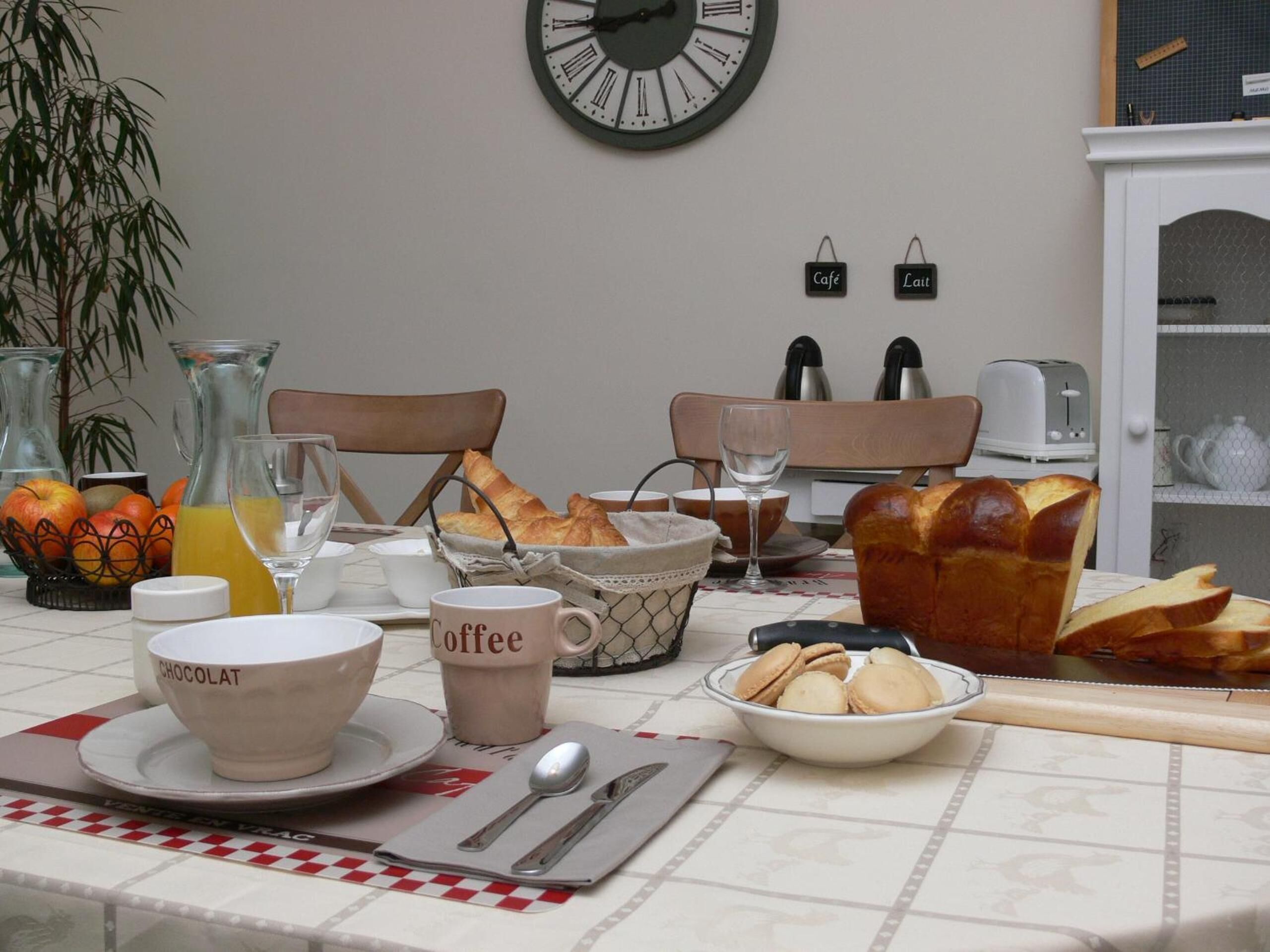 A breakfast table with croissants, a coffee mug, and a bowl of macarons.