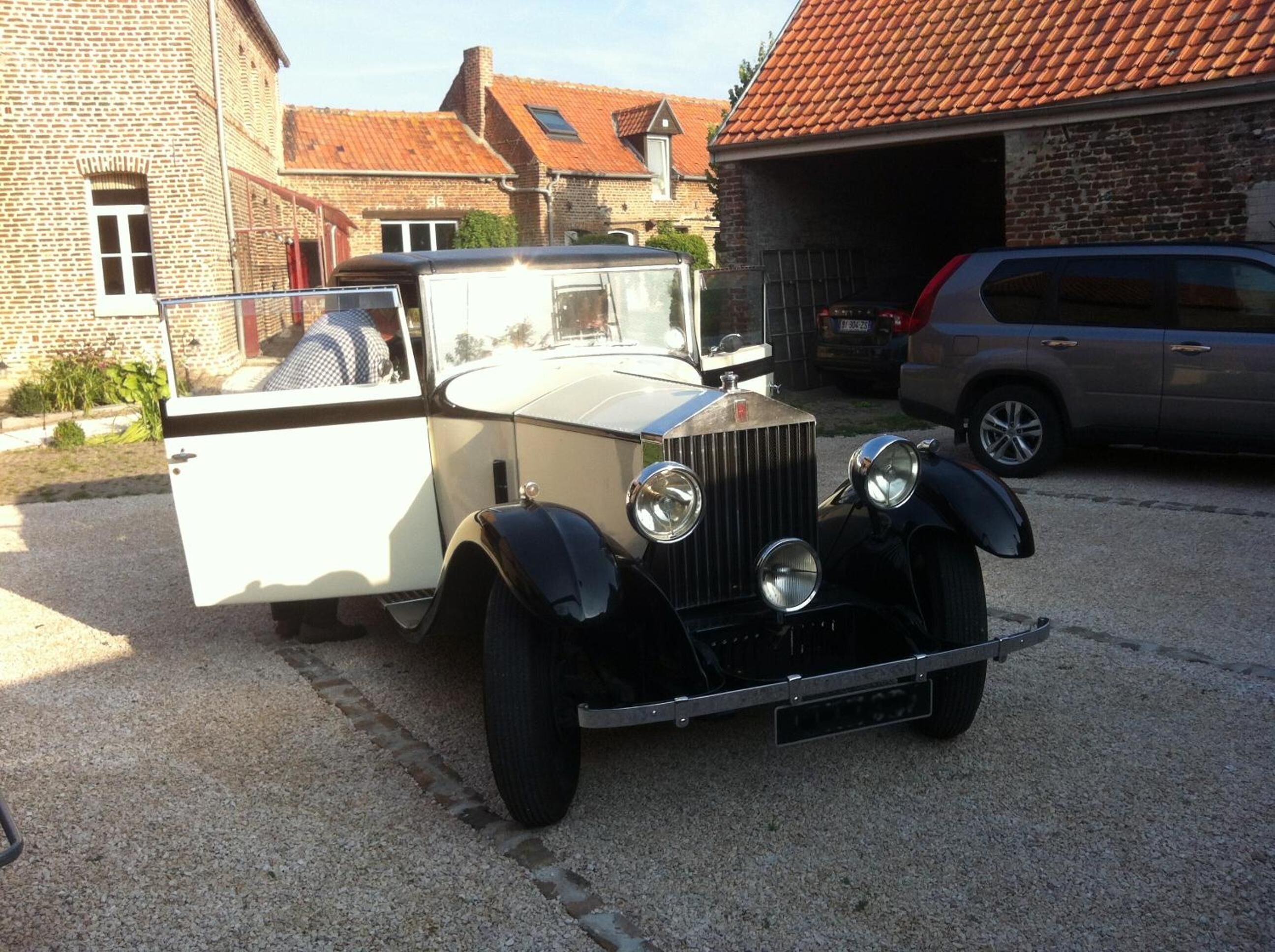 A vintage car parked in a driveway with a brick building and a garage in the background.