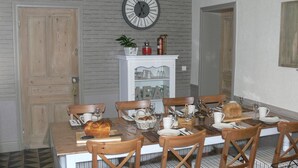A dining room with a wooden table set for six, surrounded by six wooden chairs with striped cushions. A white cabinet with glass doors and a clock on the wall above the cabinet are also visible. - B&B La Ferme de l'Ostrevent (Estrées)