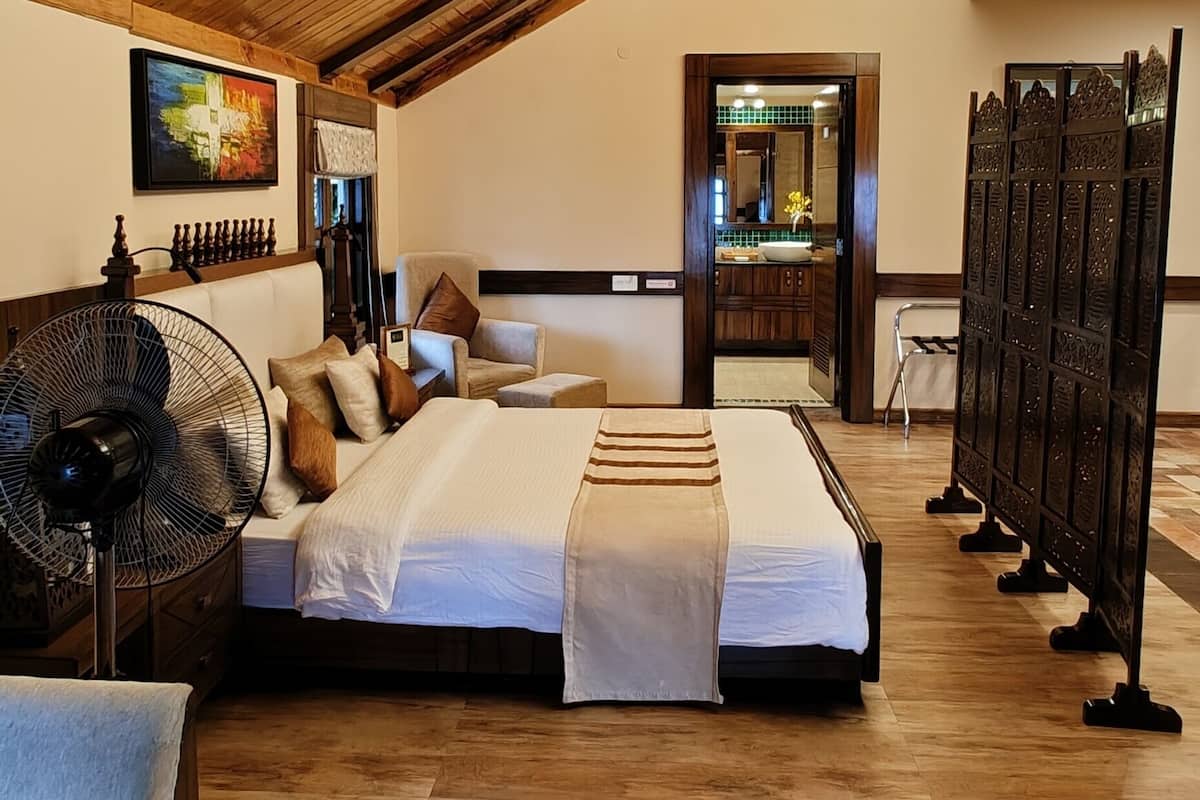 A spacious bedroom with a sloped ceiling, a large bed, a sitting area with a fan, and a view of the bathroom.