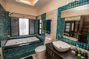 Ein Badezimmer mit Badewanne, Toilette, Waschbecken und einem Fenster mit Jalousien.