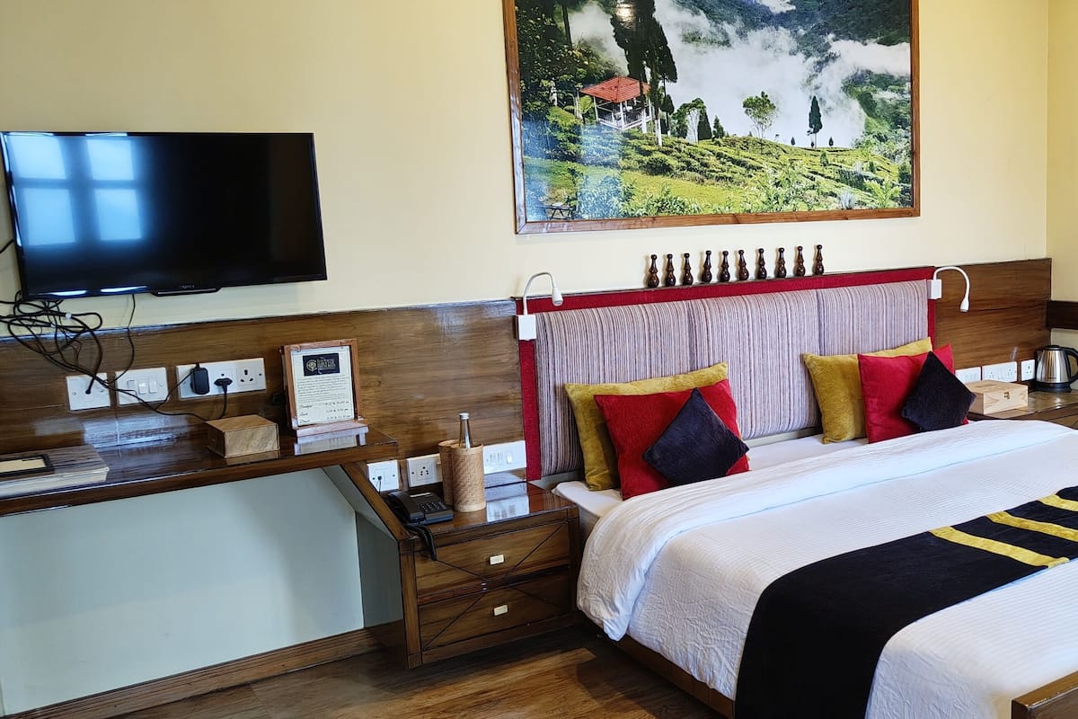 A hotel room with a bed, bedside tables, a TV, and a painting on the wall.