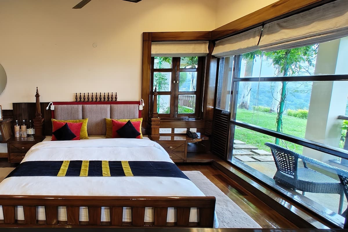 A spacious bedroom with a large bed, a red armchair, and a view of the outdoors through large windows.