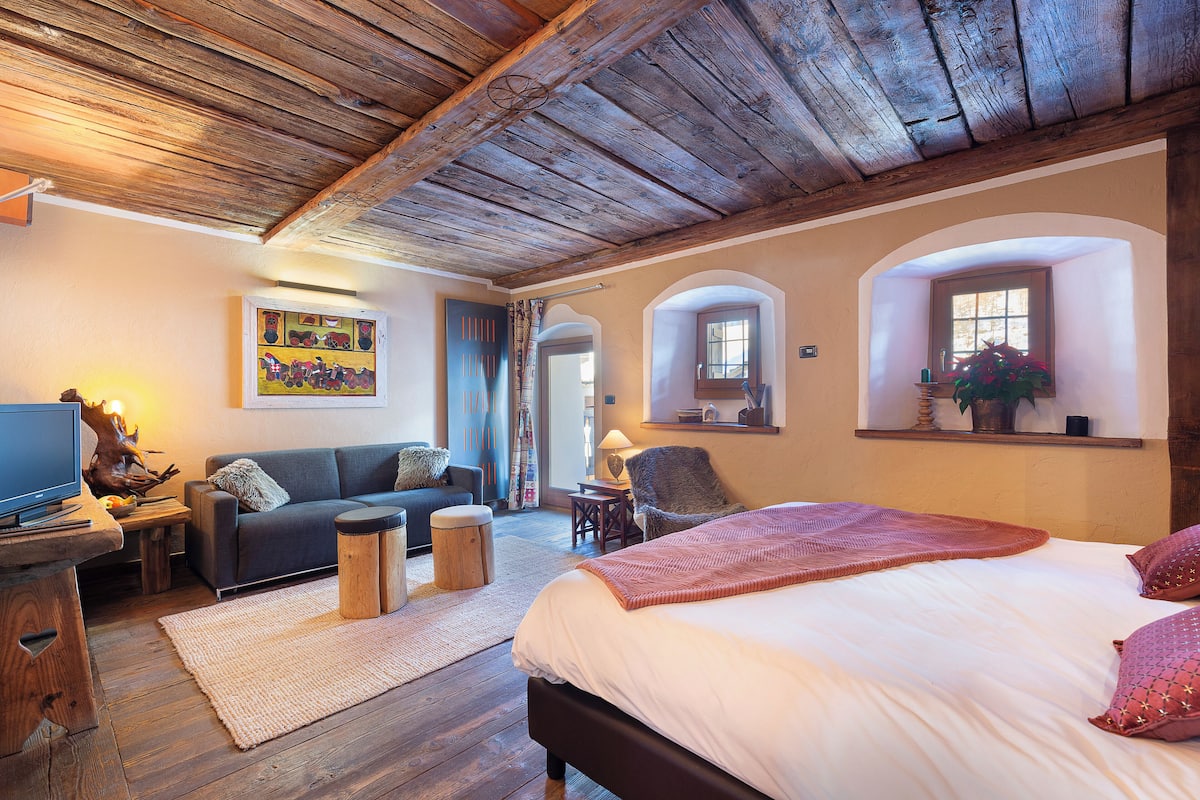 Een gezellige kamer met een bed, een slaapbank, een televisie en een houten plafond.