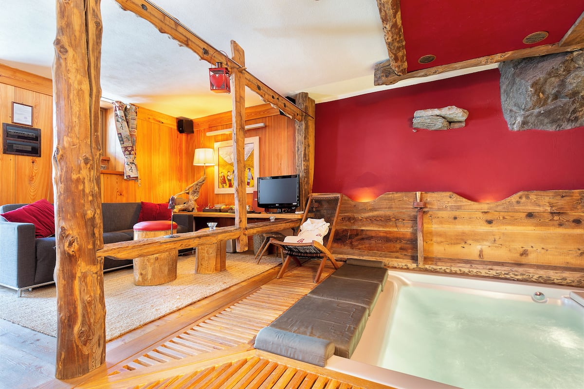 Een houten interieur met een rode wand, een houten bankje, een bank, een televisie en een bad.