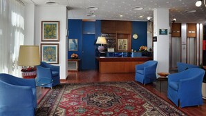 Vestíbulo de hotel con sillones azules, una recepción, una alfombra estampada y obras de arte en las paredes.