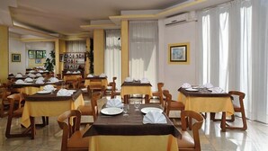 Un comedor de hotel con varias mesas dispuestas para comer, sillas y un amplio ventanal con cortinas.