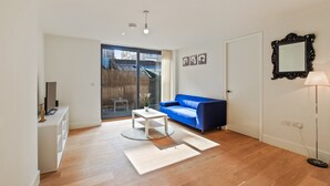 Uma sala de estar moderna com um sofá azul, uma mesa de centro branca e um amplo painel de vidro deslizante que dá para uma varanda.