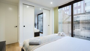 Quarto de hotel moderno com uma cama grande, guarda-roupa, espelho de banheiro e vista para o exterior.