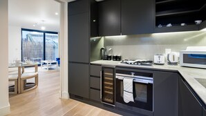 Cozinha moderna com armários escuros, forno embutido e bancada com cafeteira e torradeira.
