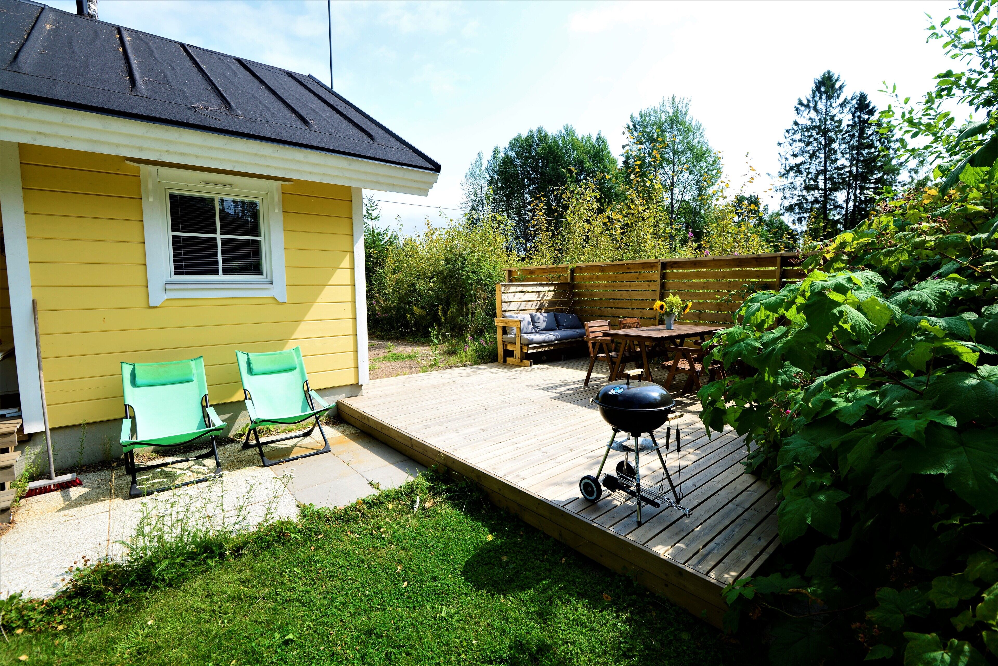 A yellow house with a deck, two green chairs, a table, and a grill.