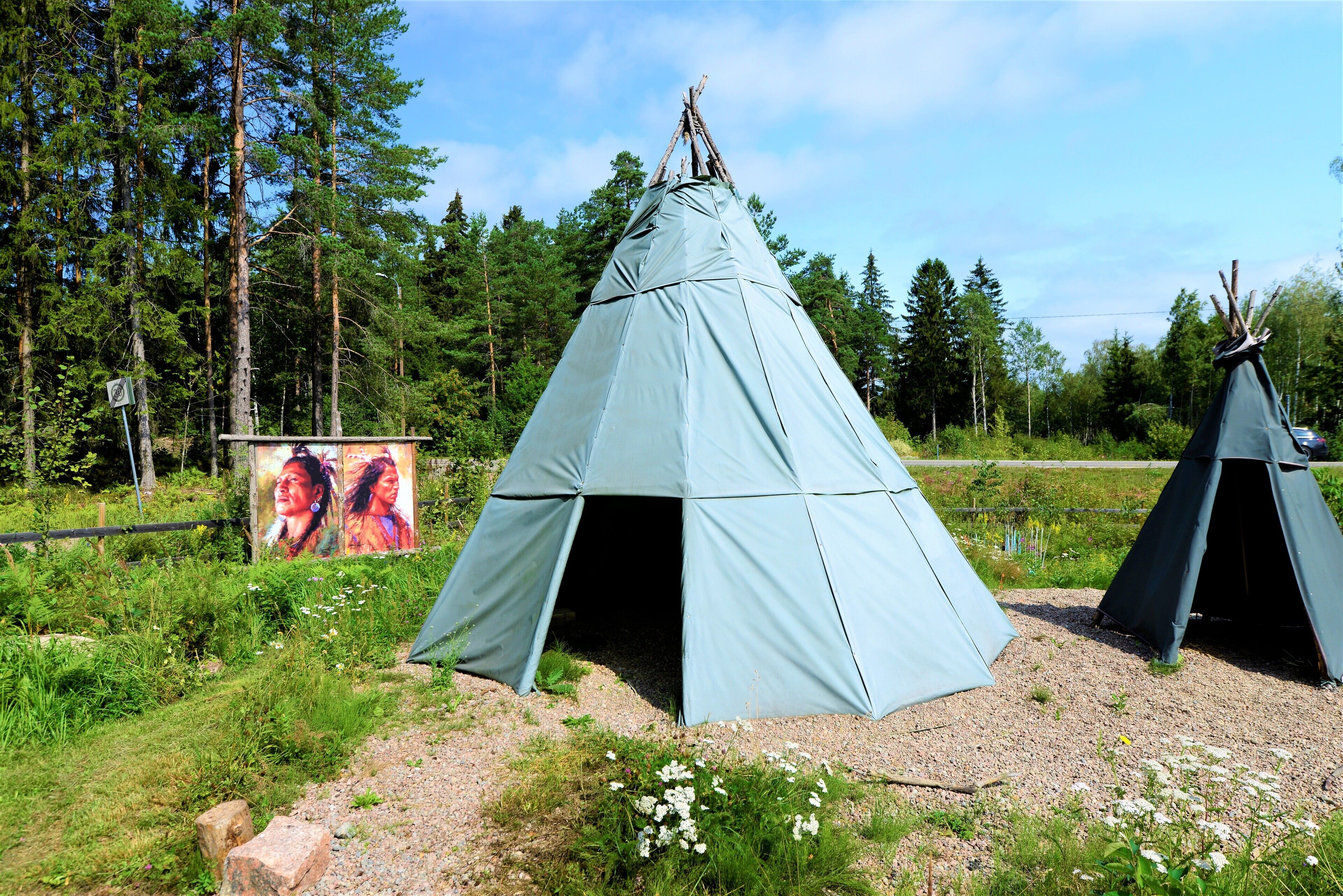 A large, light blue teepee with a simple design, surrounded by a natural forest setting.