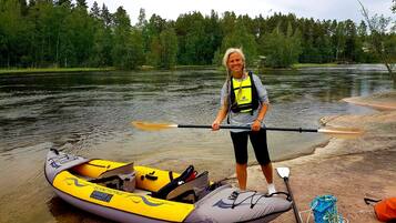 A person standing next to a yellow and gray kayak on a riverbank.