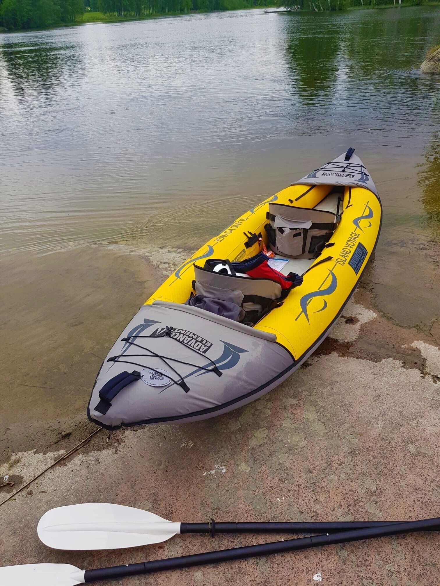 Ein gelbes Kajak mit der Aufschrift "ADVANCEMENT" und "ISLAND VOYAGE", das auf einer Betonfläche in der Nähe von Wasser liegt.