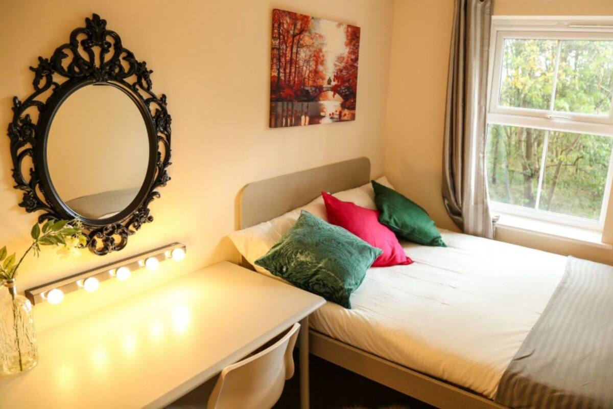A bedroom with a bed, bedside table, mirror, and a window with curtains.