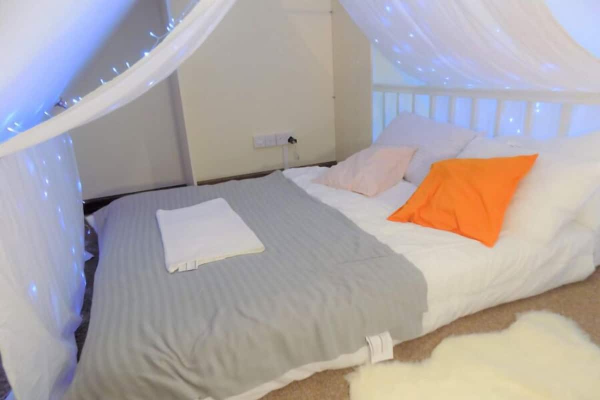 A bed with a grey bedspread, white pillows, and an orange pillow.