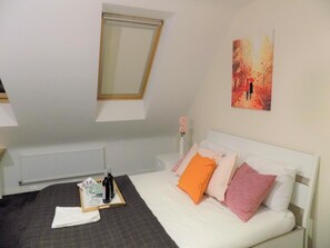 A bedroom with a bed, a window, a radiator, a painting, and a tray with wine bottles and glasses. - Casa Homestay (Coventry)