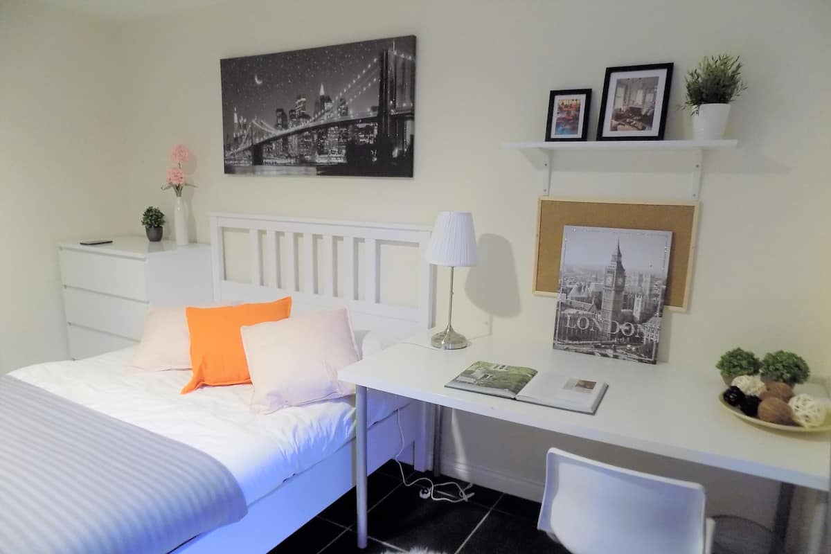 A neatly arranged bedroom with a bed, bedside table, lamp, and a cityscape picture on the wall.