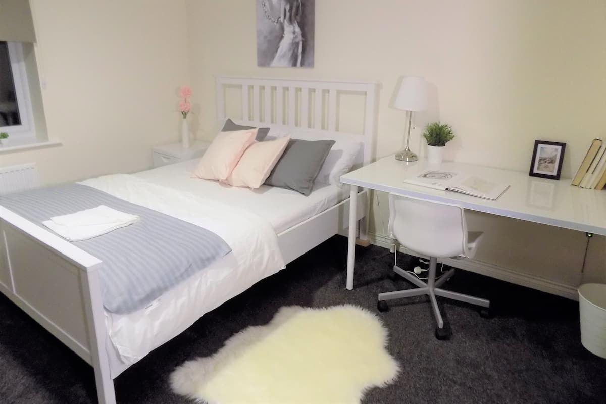 A neatly arranged bedroom with a bed, bedside table, desk, chair, and a small potted plant.