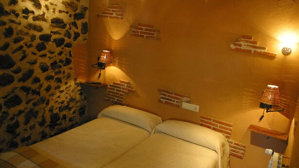 A bedroom with a stone wall, a brick-patterned wall, and two bedside lamps. - Posada de Bleto (Ledesma)