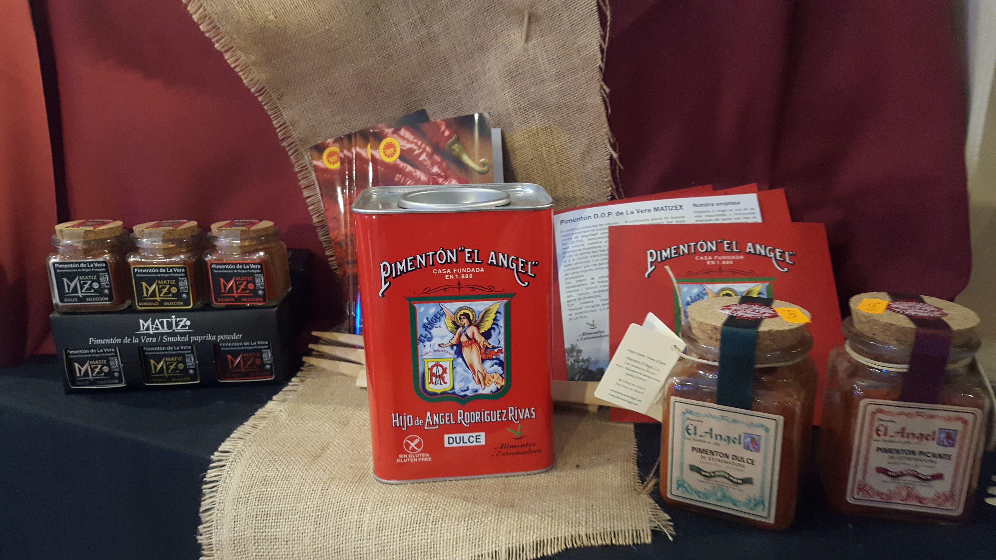A display of MATIZ brand products including jars of pimentón dulce, a can of pimentón el angel, and a booklet.