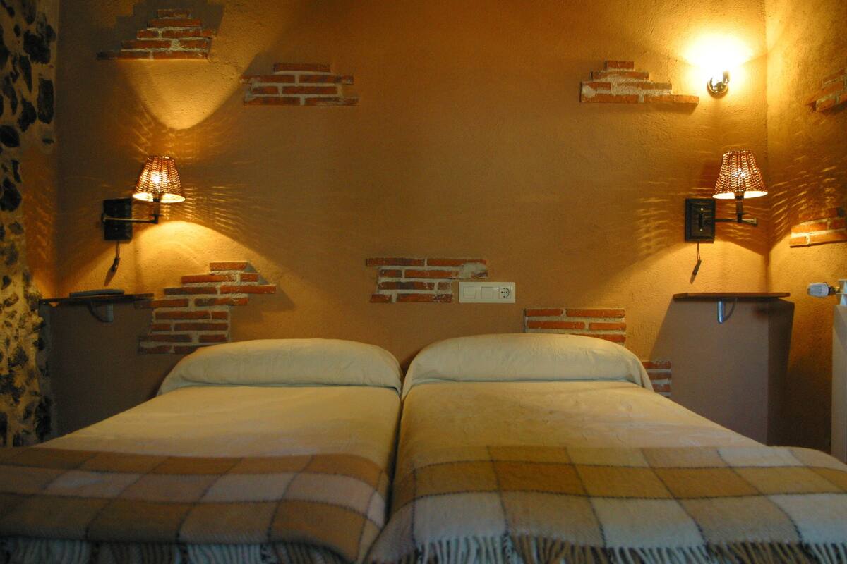 Une chambre avec deux lits, des murs en briques apparentes et des lampes fixées au mur.