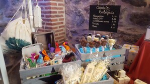 A chocolate shop with a rustic brick wall background, displaying various chocolate products and a menu board listing prices. - Posada de Bleto (Ledesma)