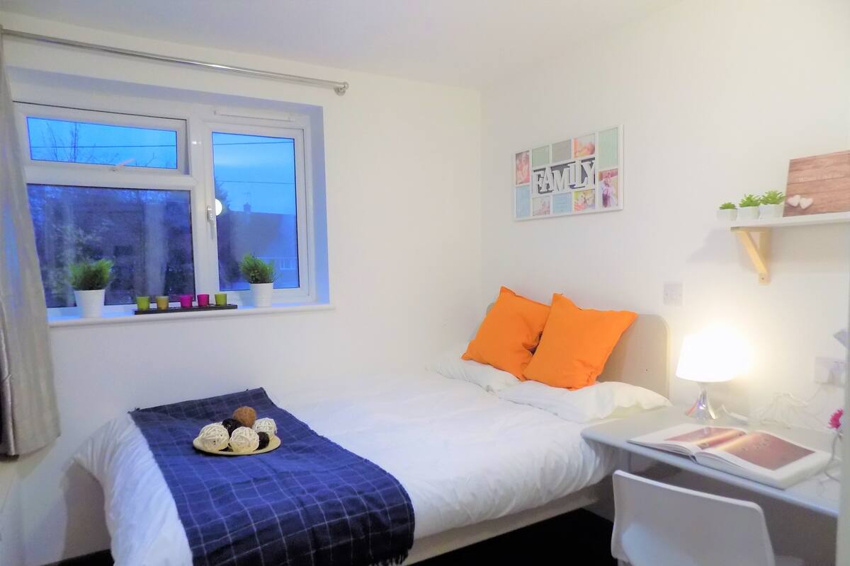 A bedroom with a bed, a desk, and a window.