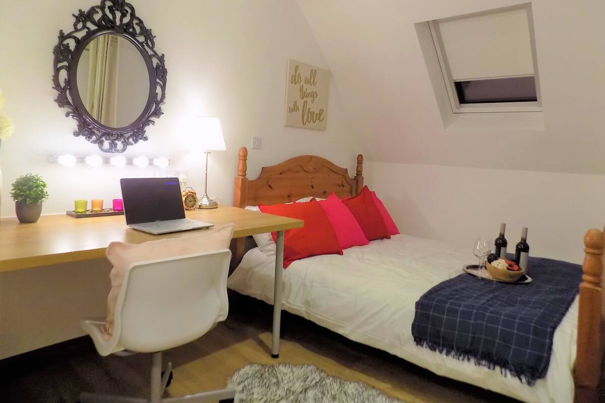 A bedroom with a wooden bed, a desk with a laptop, a mirror, bedside lamps, and a motivational poster.