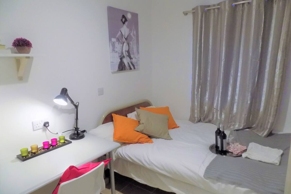 A bedroom with a bed, a desk, a chair, a lamp, and a poster on the wall.