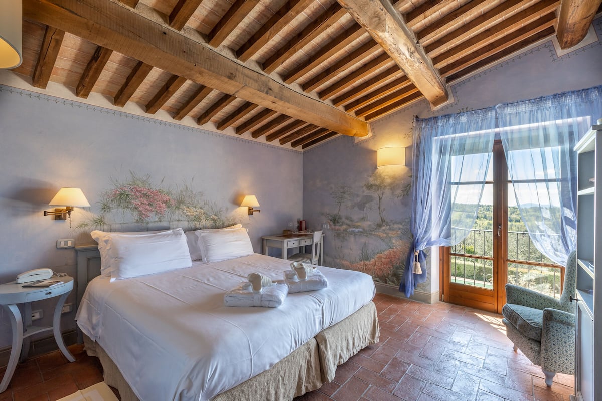 Un dormitorio con una cama grande, dos mesitas de noche, un escritorio, una silla y una ventana con cortinas.