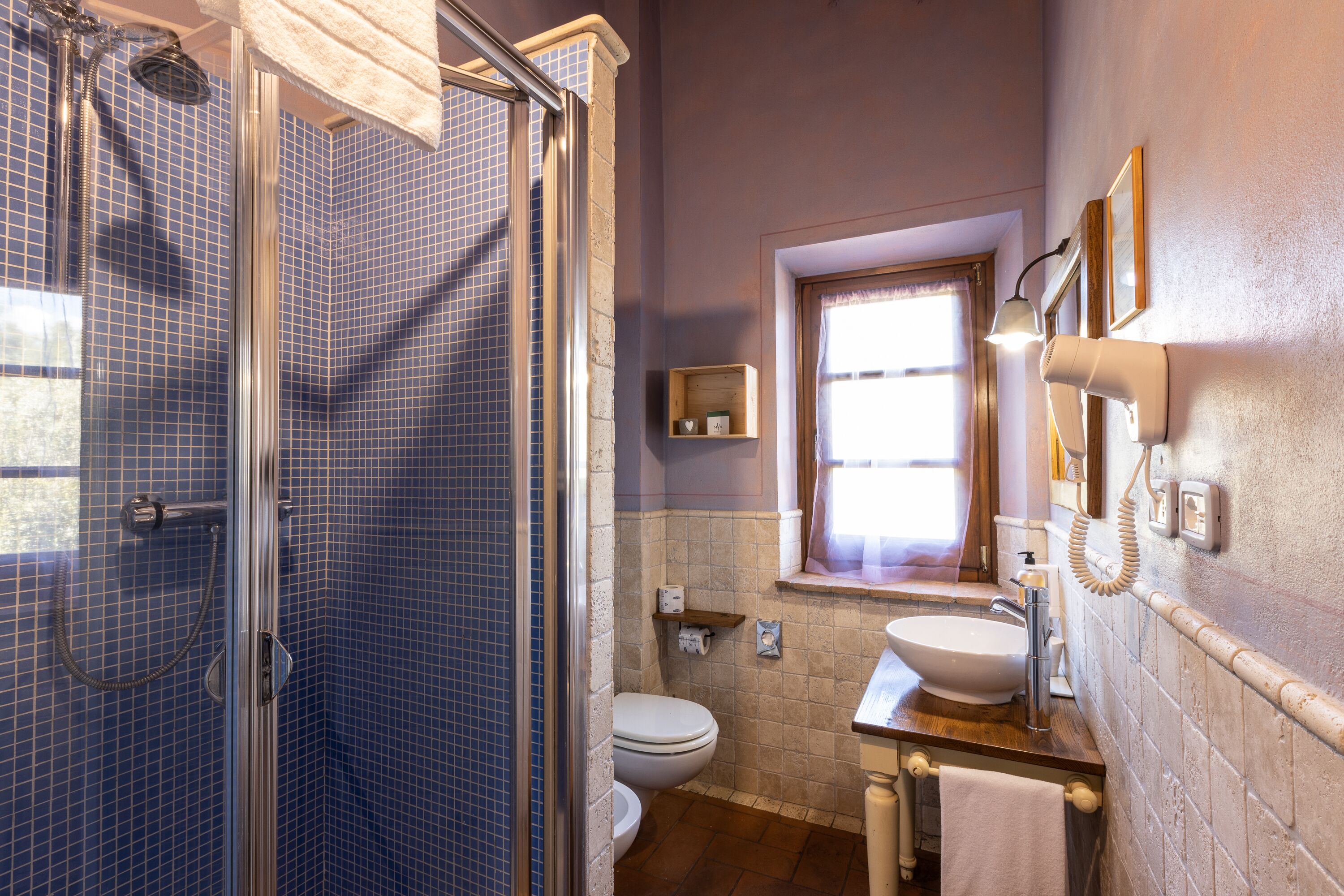 A bathroom with a glass shower enclosure, a toilet, a sink, and a window.