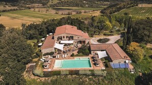 Une grande maison en pierre dotée d’une piscine, entourée d’une végétation luxuriante et de collines.