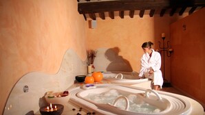 Un espace spa comprenant deux bains à remous, un récipient décoratif avec des bougies et une personne portant un peignoir.