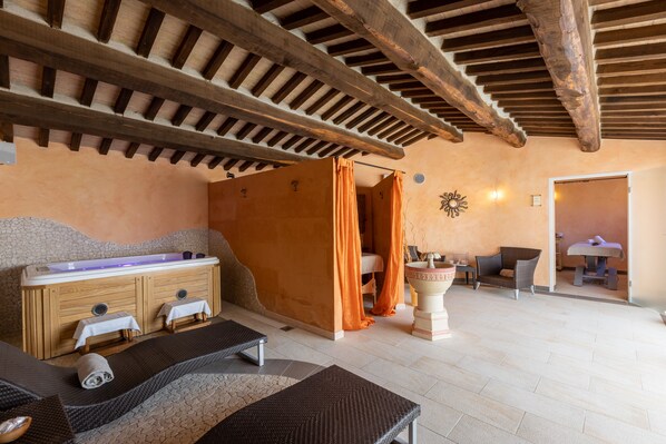 A spa room with a wooden ceiling, a massage table, a bathtub, and a chair. - La Melosa Resort & Spa - Adults Only (Roccastrada)