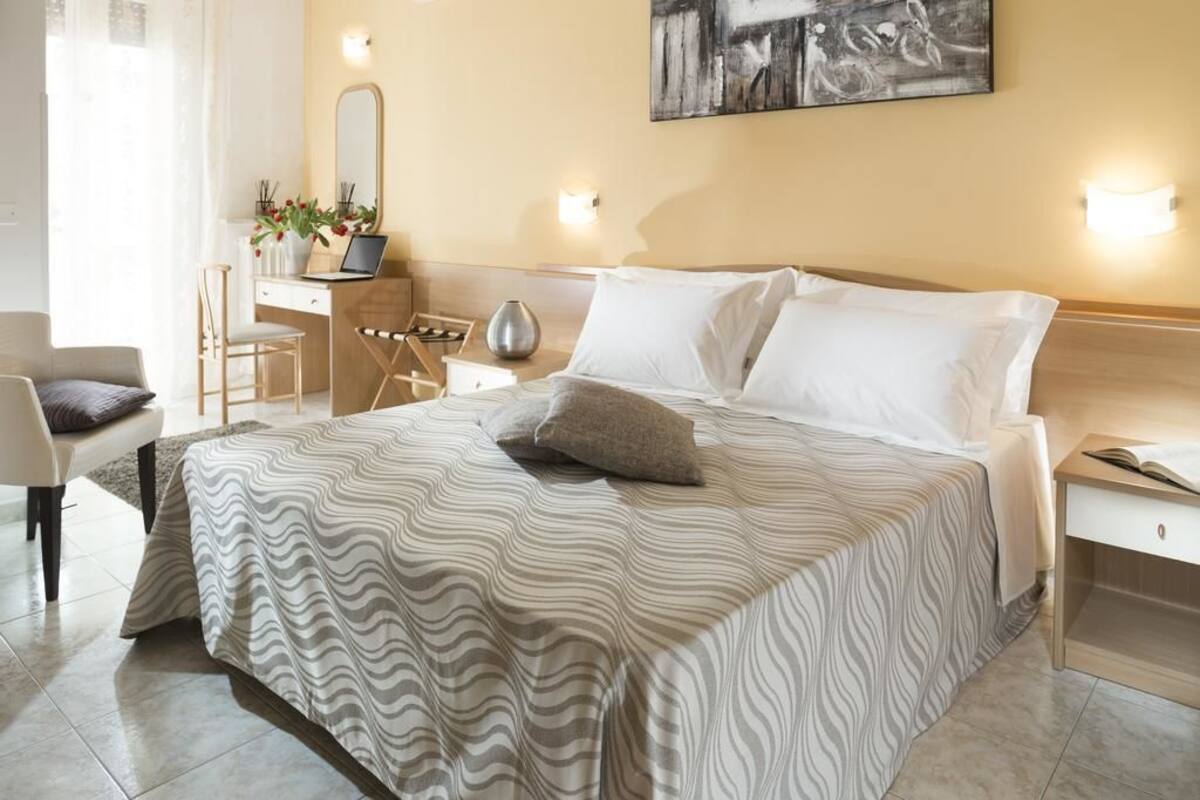 A neatly arranged bedroom with a bed, bedside table, chair, desk, and a mirror.