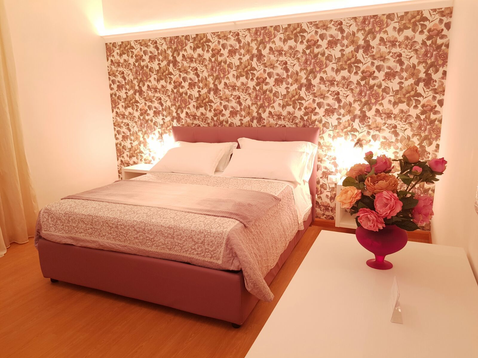 A neatly arranged bedroom with a bed, a nightstand, and a vase of flowers.