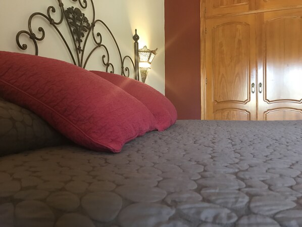 Una cama con una colcha estampada y dos almohadas rojas.