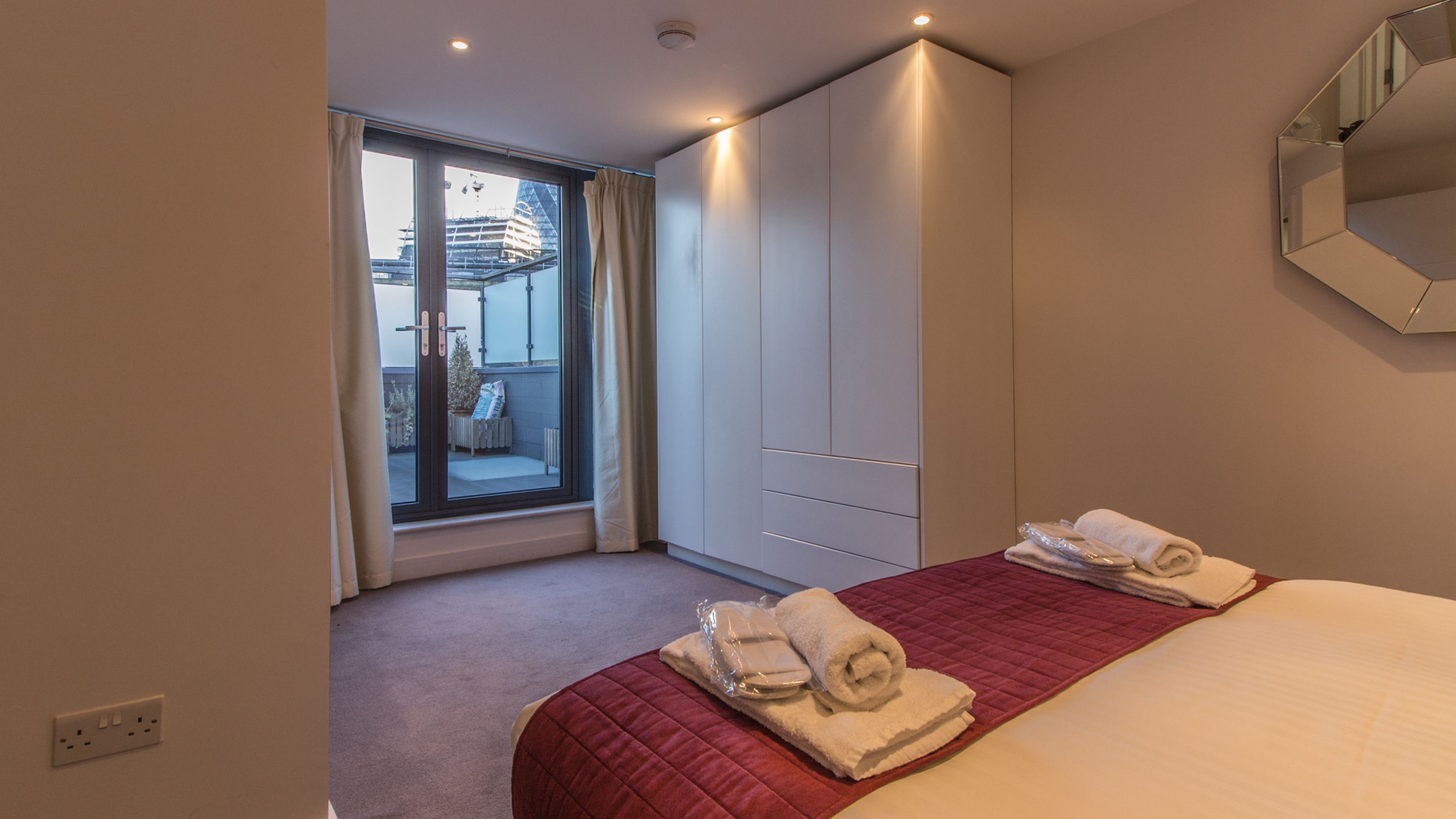 A hotel room with a large bed, a wardrobe, a window with curtains, and a view of a building outside.