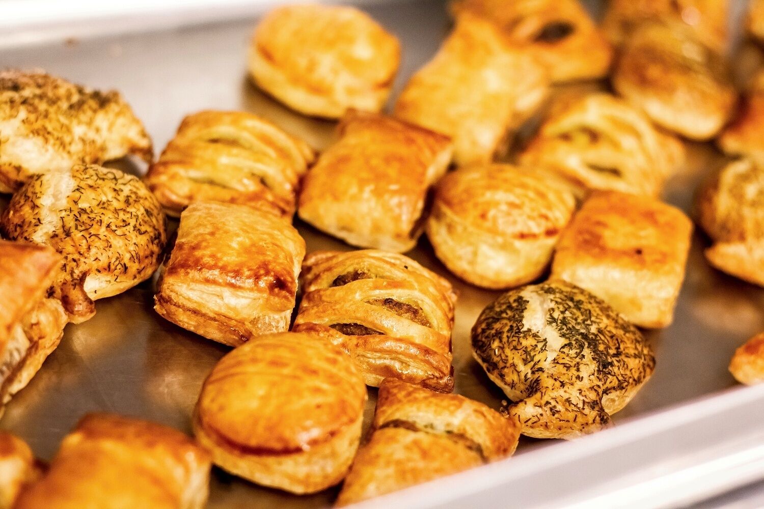 Uma bandeja de pastéis assados, provavelmente salgados, com crosta dourada e ervas visíveis.