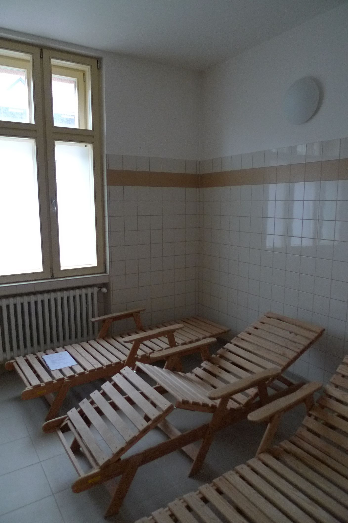 A room with white tiled walls, a window with blinds, and several wooden benches.