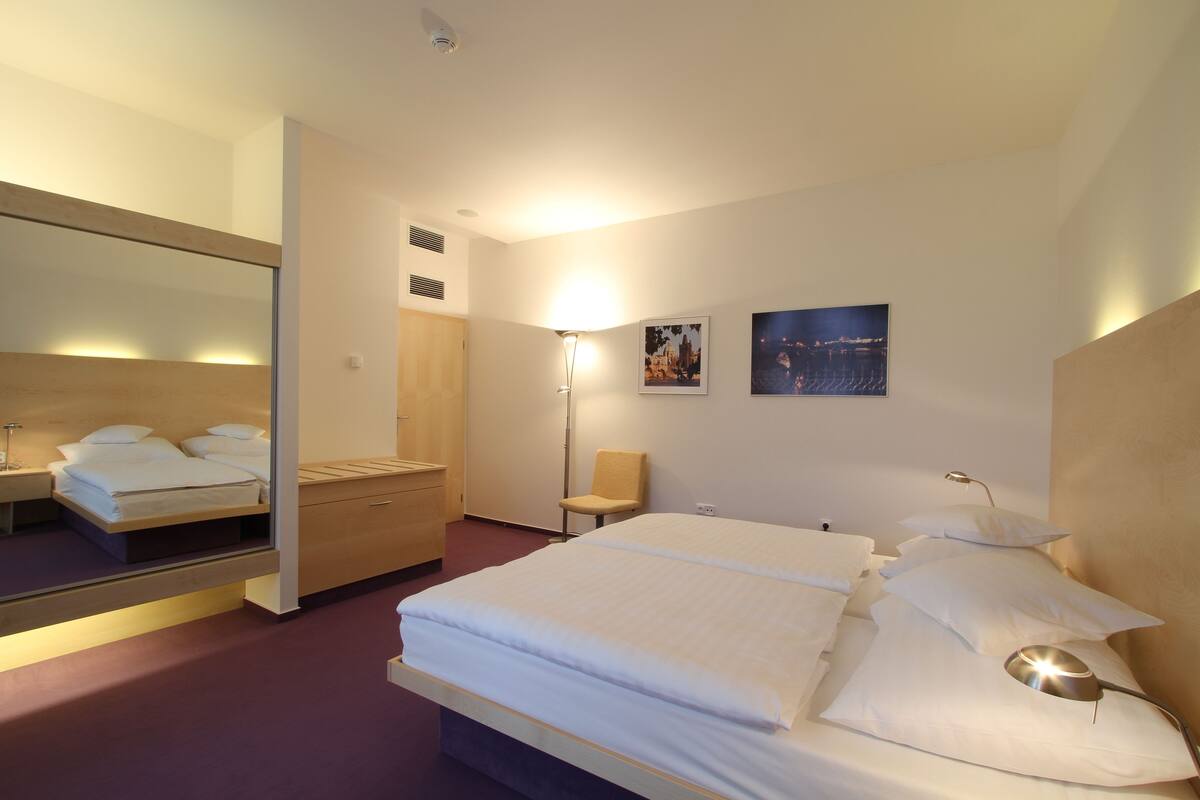 Habitación de hotel con una cama grande, una mesita de noche, una silla, un espejo y dos cuadros colgados en la pared.