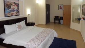 Ein Hotelzimmer mit einem Bett, einem Schreibtisch und einem Stuhl. Ein Gemälde hängt an der Wand und eine Tür führt in einen anderen Raum.