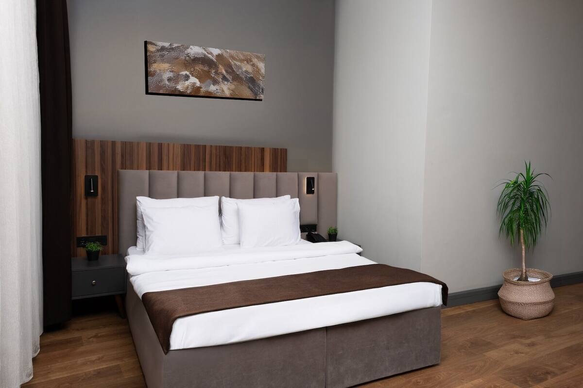 A modern bedroom with a bed, a headboard, bedside tables, a wall-mounted artwork, and a potted plant.